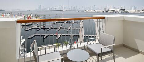A balcony with two chairs and a table, overlooking a marina and a city skyline.