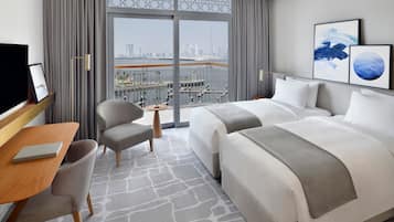 Une chambre d’hôtel avec un grand lit, un bureau avec une chaise, une petite table et une vue sur la ville grâce à de grandes fenêtres.