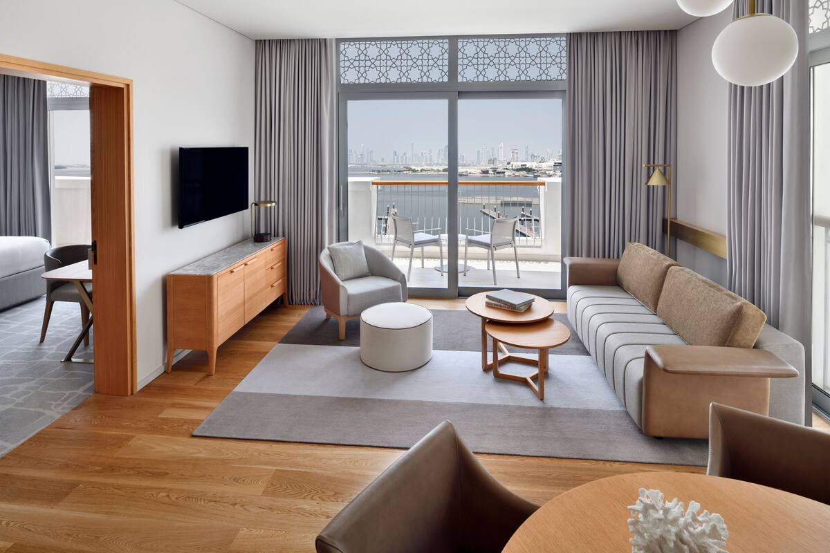 A modern living room with a sofa, chairs, a TV, and a balcony with a city view.