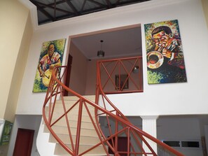 A staircase with red railings leading to an upper floor. There are two paintings on the walls, one depicting a person playing a drum and the other a person playing a trumpet. - TS Lodgings (Accra)