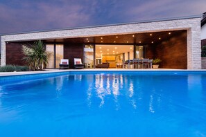 Una casa moderna con piscina, un patio y un amplio ventanal que da al interior.