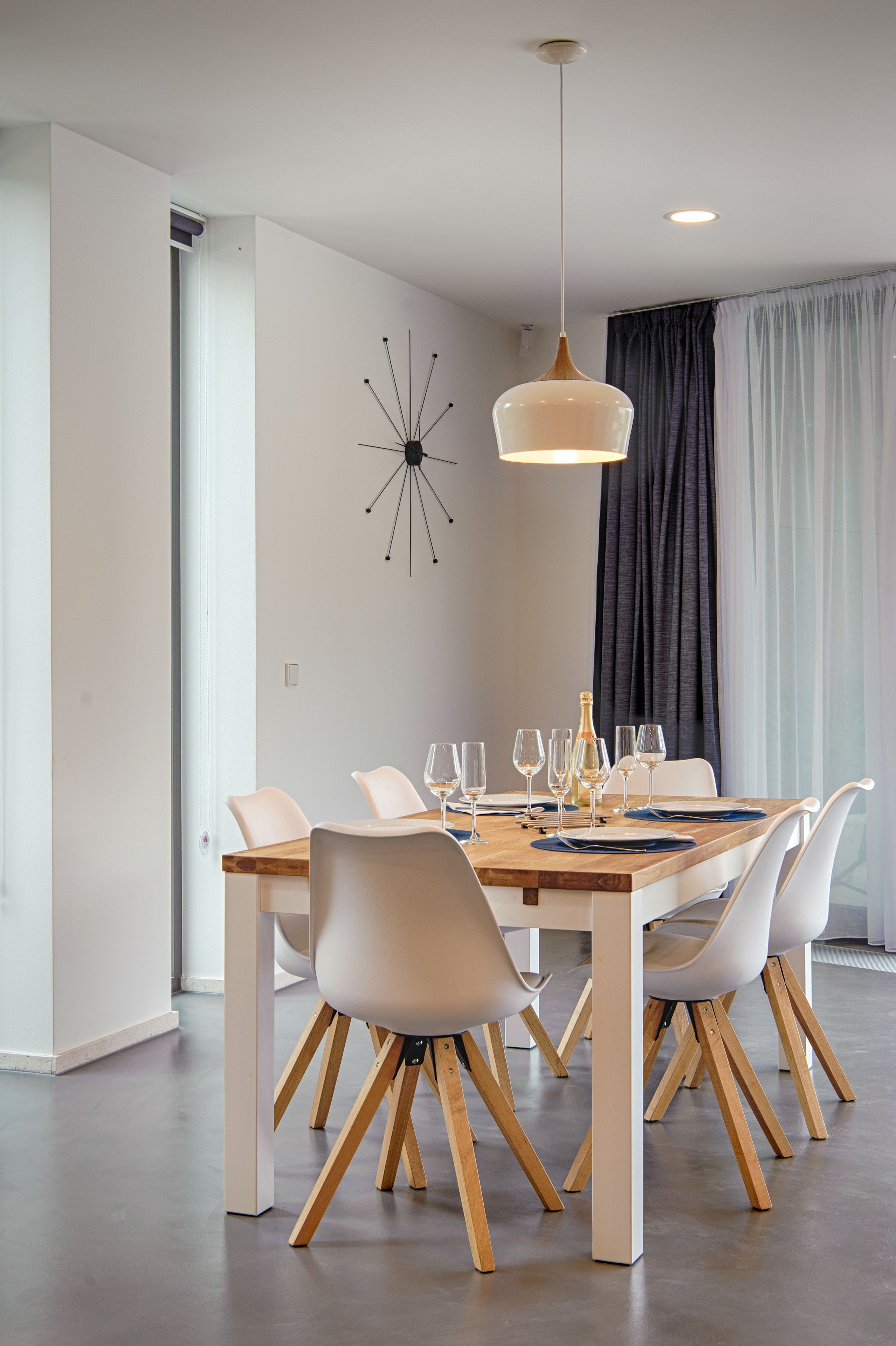 A modern dining area with a wooden table, white chairs, and a pendant light.