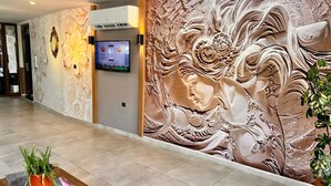 A lobby with a marble-patterned wall, a mounted TV, a wooden reception desk, and a potted plant. - Hayal Residence Apart Otel (Antalya)
