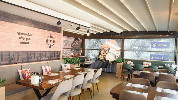 A modern cafe with wooden tables, cushioned seating, and a wall with motivational text. - Hayal Residence Apart Otel (Antalya)