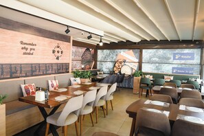 Un café moderno con mesas de madera, asientos acolchados y una pared con mensajes inspiradores.