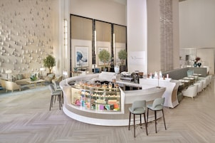 A modern hotel lobby with a central bar area, seating arrangements, and a decorative wall.