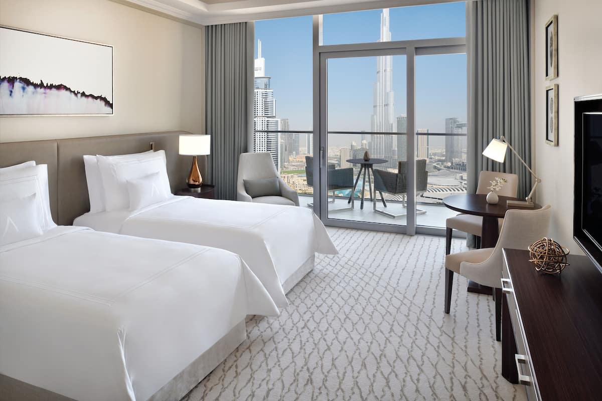 A hotel room with two beds, a desk, a chair, a TV, and a balcony with a city view.