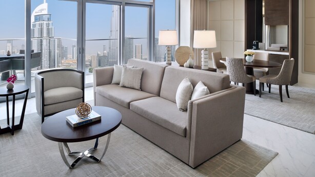 Ein modernes Hotelzimmer mit einem großen Fenster und Blick auf die Stadt, einer Couch, einem Couchtisch und einer Essecke mit Stühlen.
