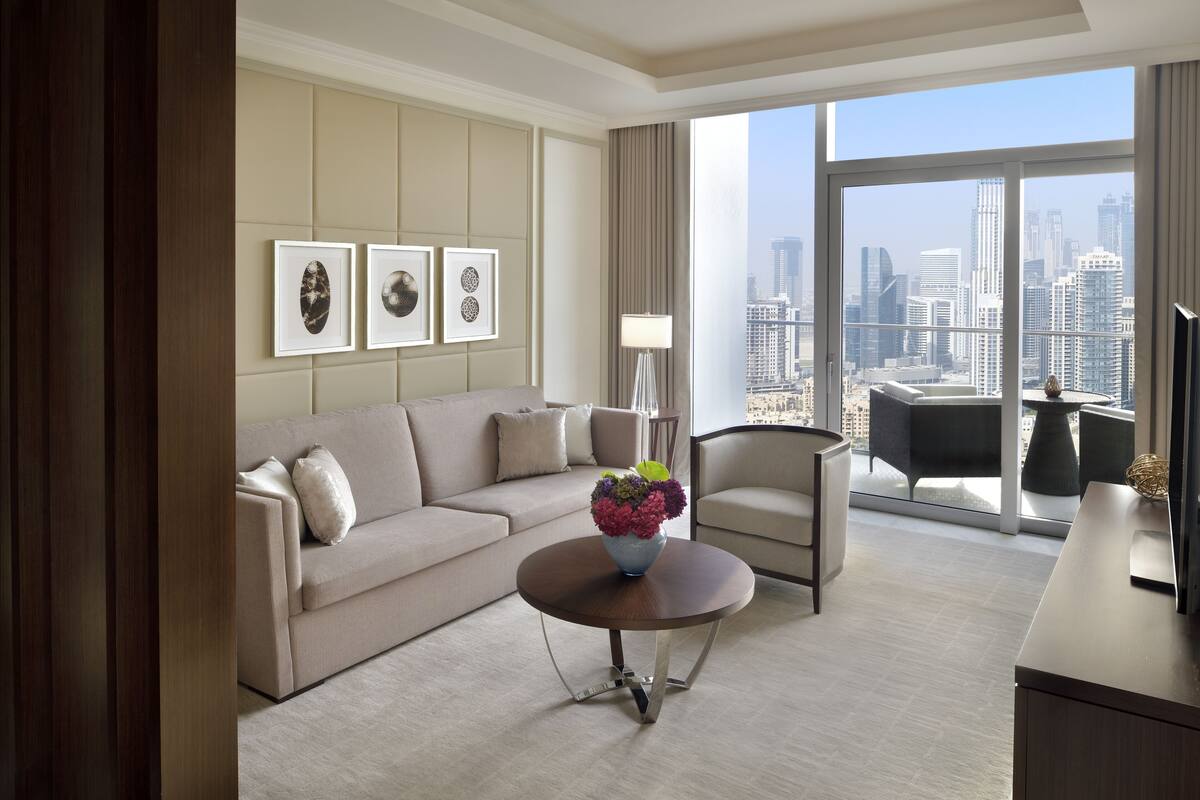 A modern hotel room with a large window, a sofa, a coffee table with a flower vase, and a city view.