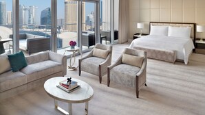 Ein Hotelzimmer mit einem großen Bett, zwei Sesseln, einem Sofa, einem kleinen Tisch mit Büchern und Blick auf die Skyline der Stadt.