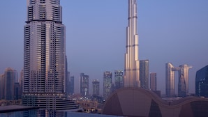 Eine moderne Skyline mit zwei markanten Wolkenkratzern, einer mit gewölbter Spitze und der andere mit Turm, die sich in einem Pool spiegeln.