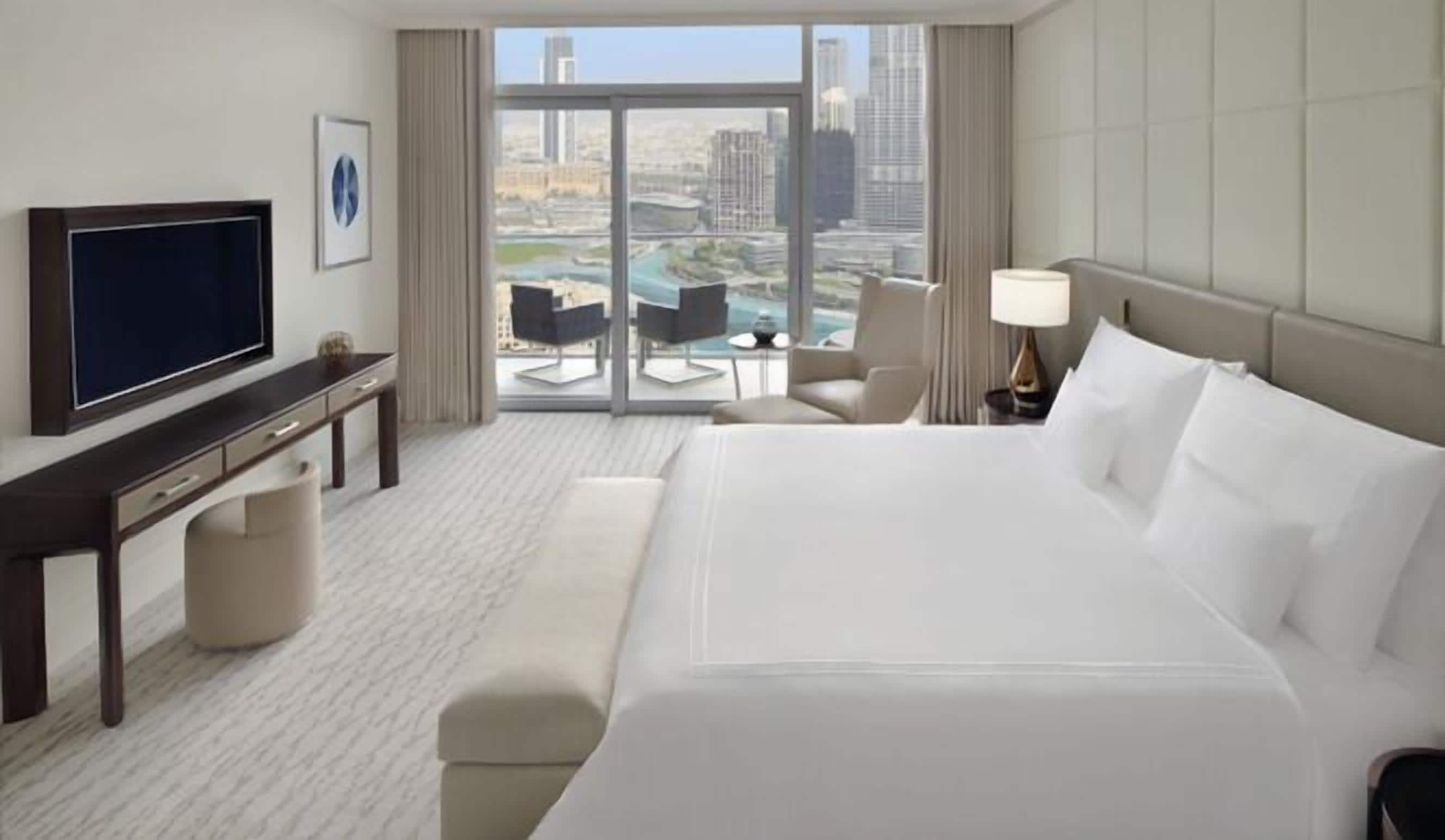 A hotel room with a large bed, a television, a desk, and a view of the city.