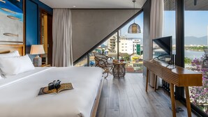 A modern hotel room with a large bed, a TV, a dining table, and a view of the city. - Seahorse Han Market Da Nang Hostel by Haviland (Da Nang)