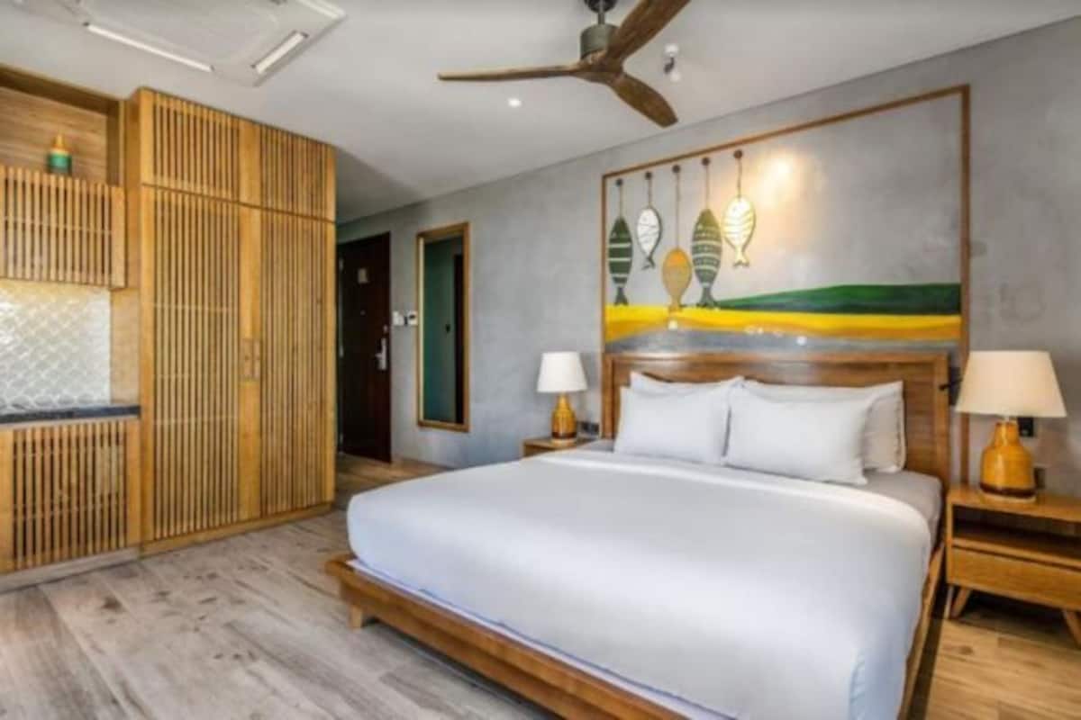 Quarto com uma cama grande, cabeceira de madeira, duas mesas de cabeceira com luminárias, um ventilador de teto e um quadro na parede.