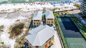Ett hotell vid stranden med tvåvåningsbyggnader, en sandstrand med parasoller och en tennisbana.
