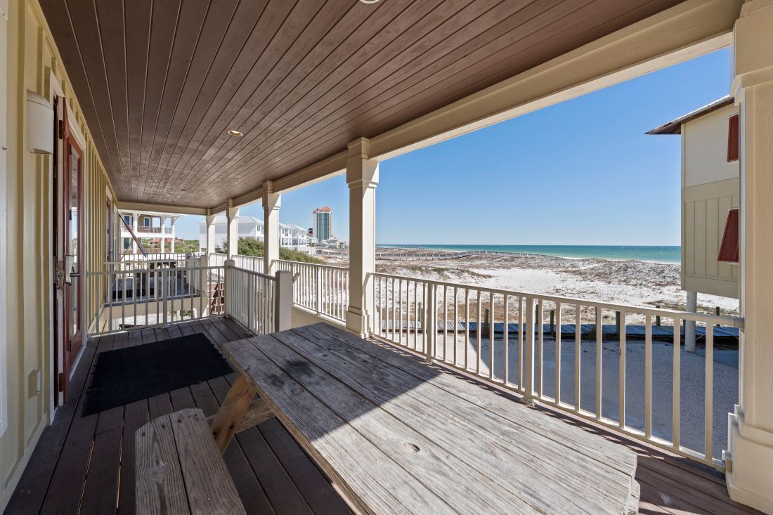 Une terrasse en bois avec un banc, des rampes blanches et une vue sur la plage et l’océan.
