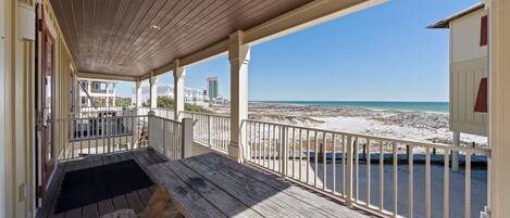Une terrasse en bois avec un banc, des rampes blanches et une vue sur la plage et l’océan.
