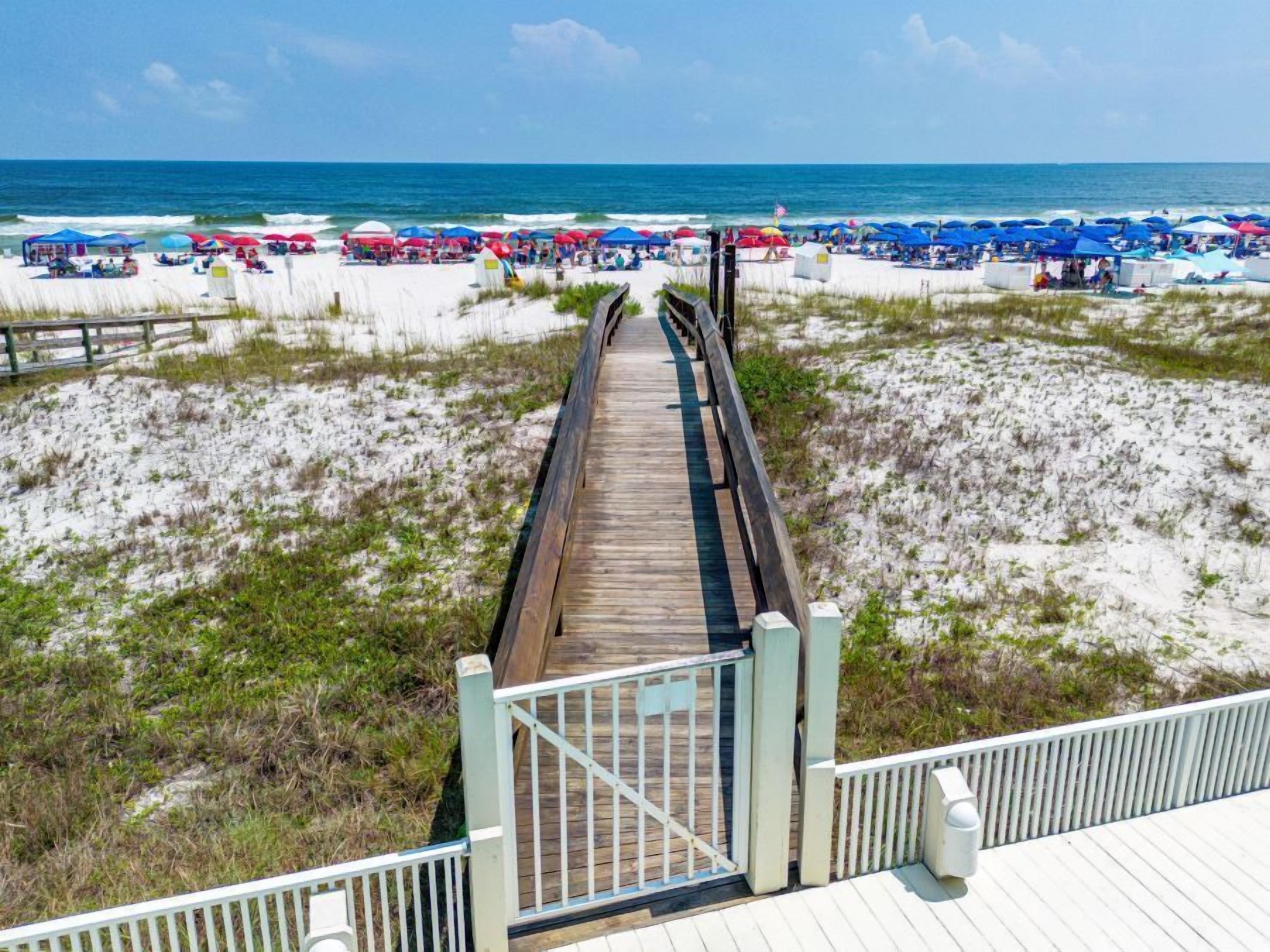 Een houten looppad naar een strand met parasols en ligbedden.