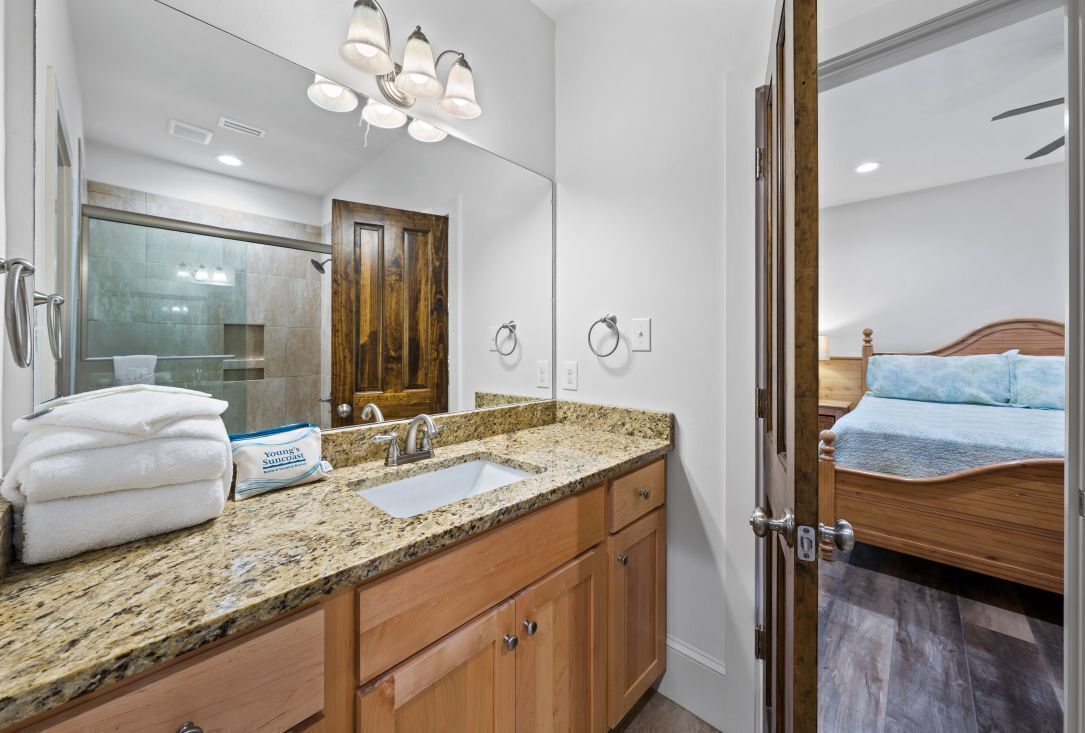 Un baño moderno con encimera de granito, armarios de madera, un espejo grande y zona de ducha.