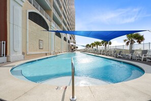 A swimming pool with a metal safety railing, surrounded by lounge chairs and a shaded area.
