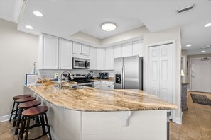 A modern kitchen with white cabinets, a granite countertop, a stainless steel refrigerator, and a microwave.