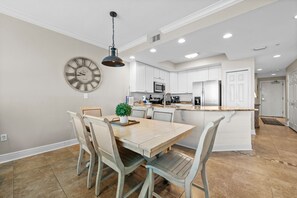 A modern kitchen with white cabinetry, a central island, and a dining area with a wooden table and chairs.