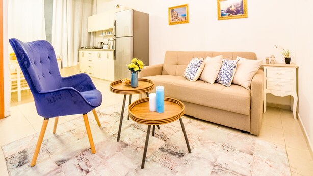 Un salon avec un canapé beige, un fauteuil bleu et deux petites tables en bois.
