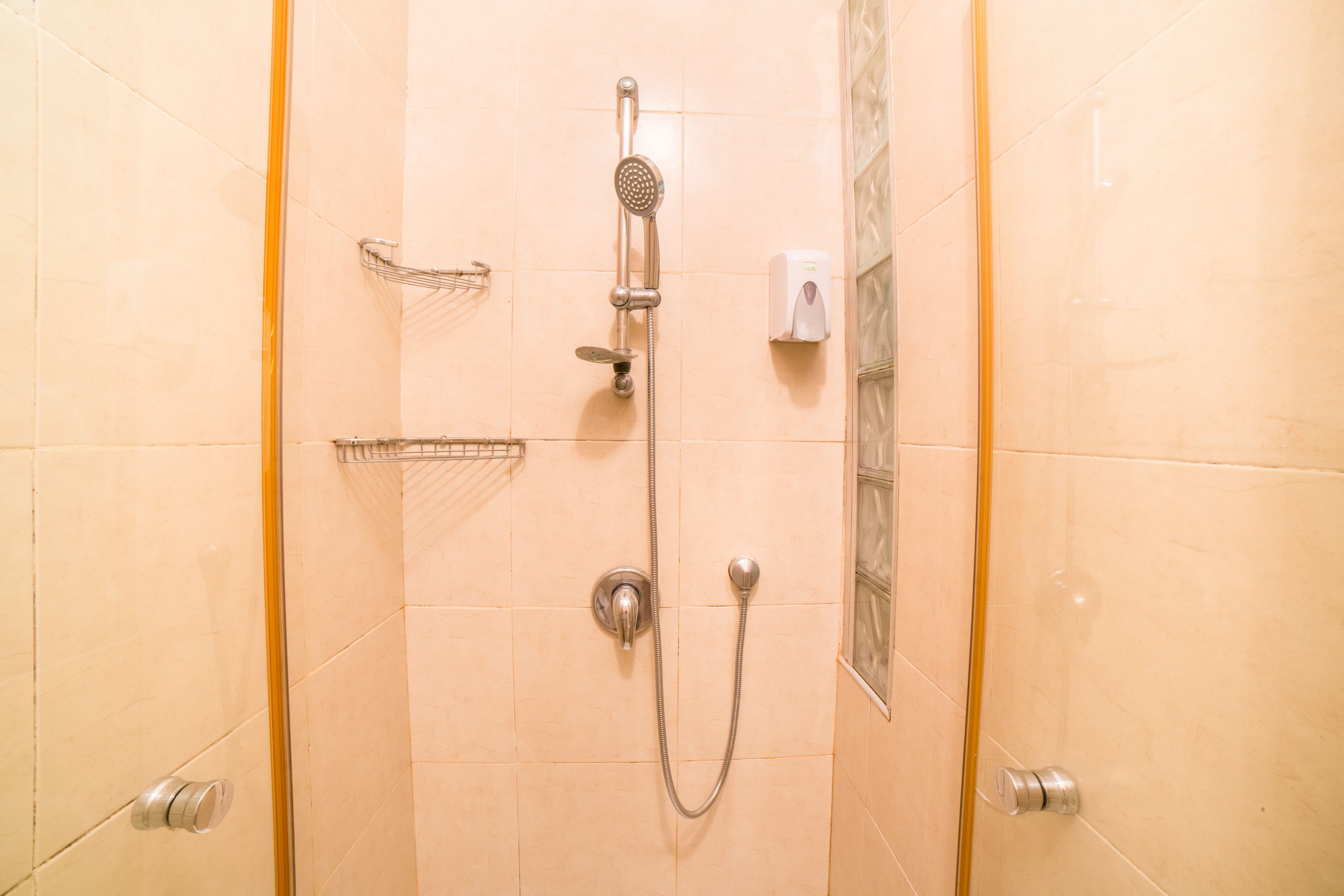 Une douche équipée d’un pommeau de douche à main, d’un robinet mural et d’un distributeur de savon.