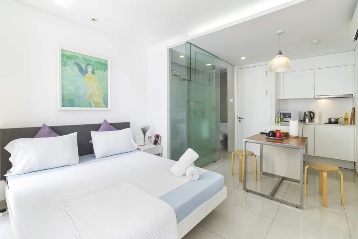 Quarto de hotel moderno com cama grande, pequena cozinha e box de vidro.
