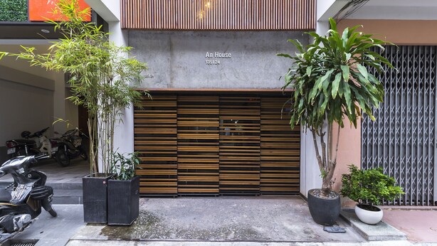 Entrada de un edificio moderno con un persiano de madera cerrado, plantas en macetas y un letrero que dice 'An House 135124'.