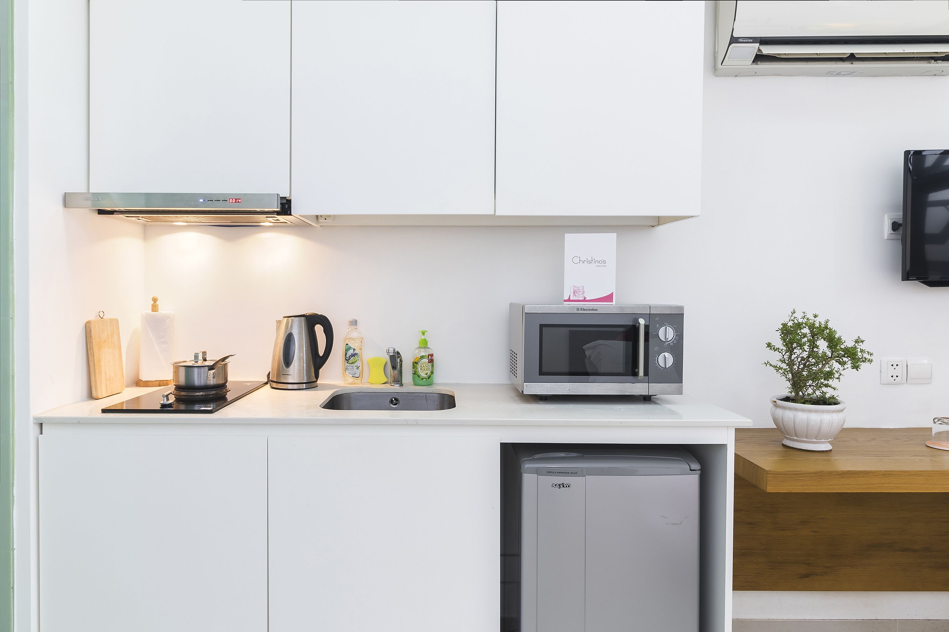 Una kitchenette compacta con microondas, hervidor, pileta y heladera pequeña.