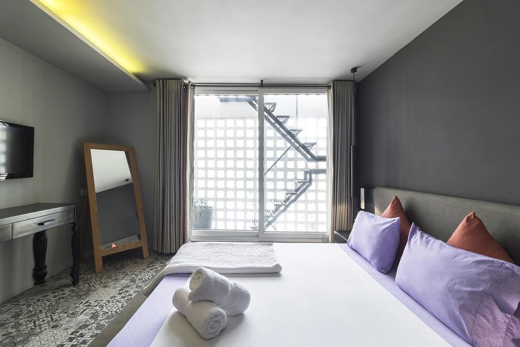 A hotel room with a bed, a desk, a chair, a TV, and a window with a view of a building.
