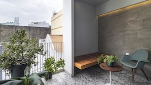 Un balcón moderno con un banco de madera, dos sillas y plantas en macetas.