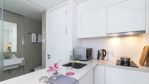 Una cocina moderna con armarios blancos, un microondas integrado, un hervidor y una estufa pequeña.