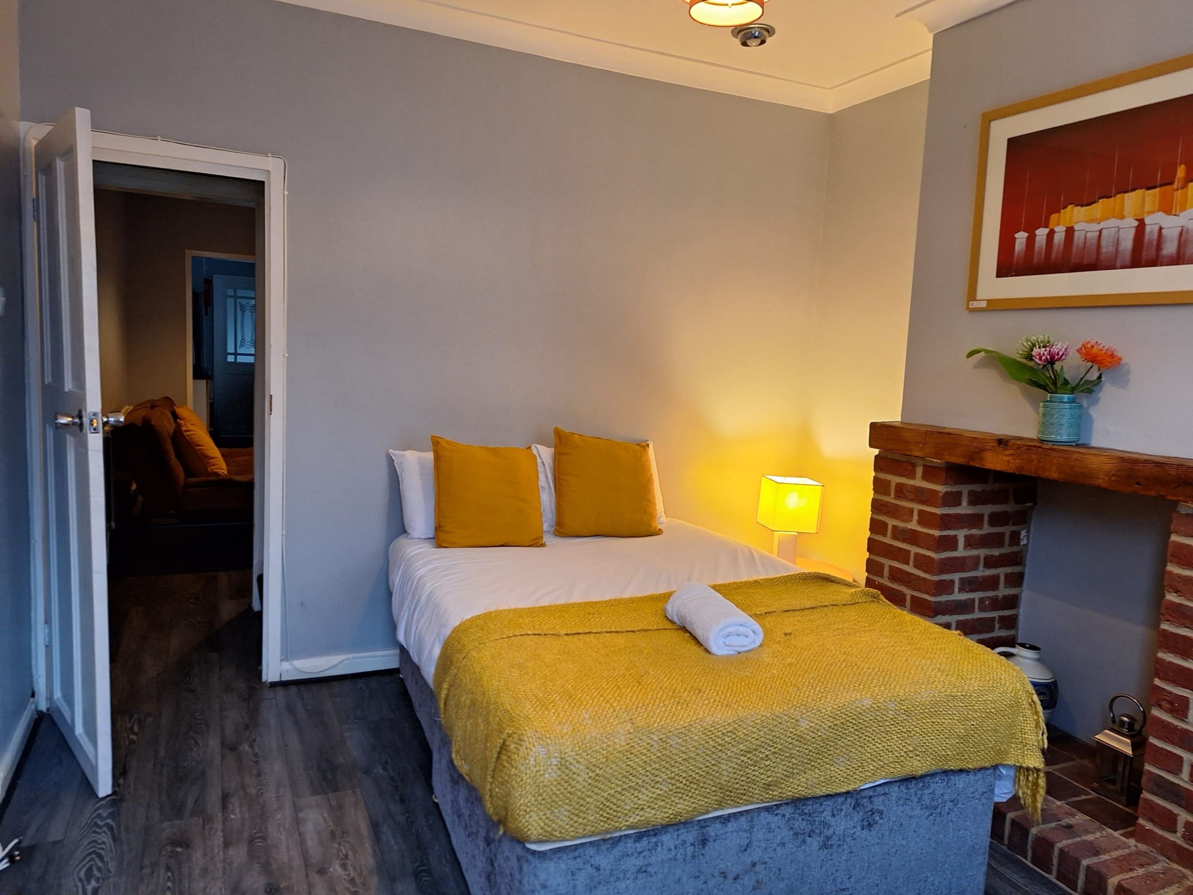 A bedroom with a bed, a yellow throw blanket, a white pillow, and a lamp.