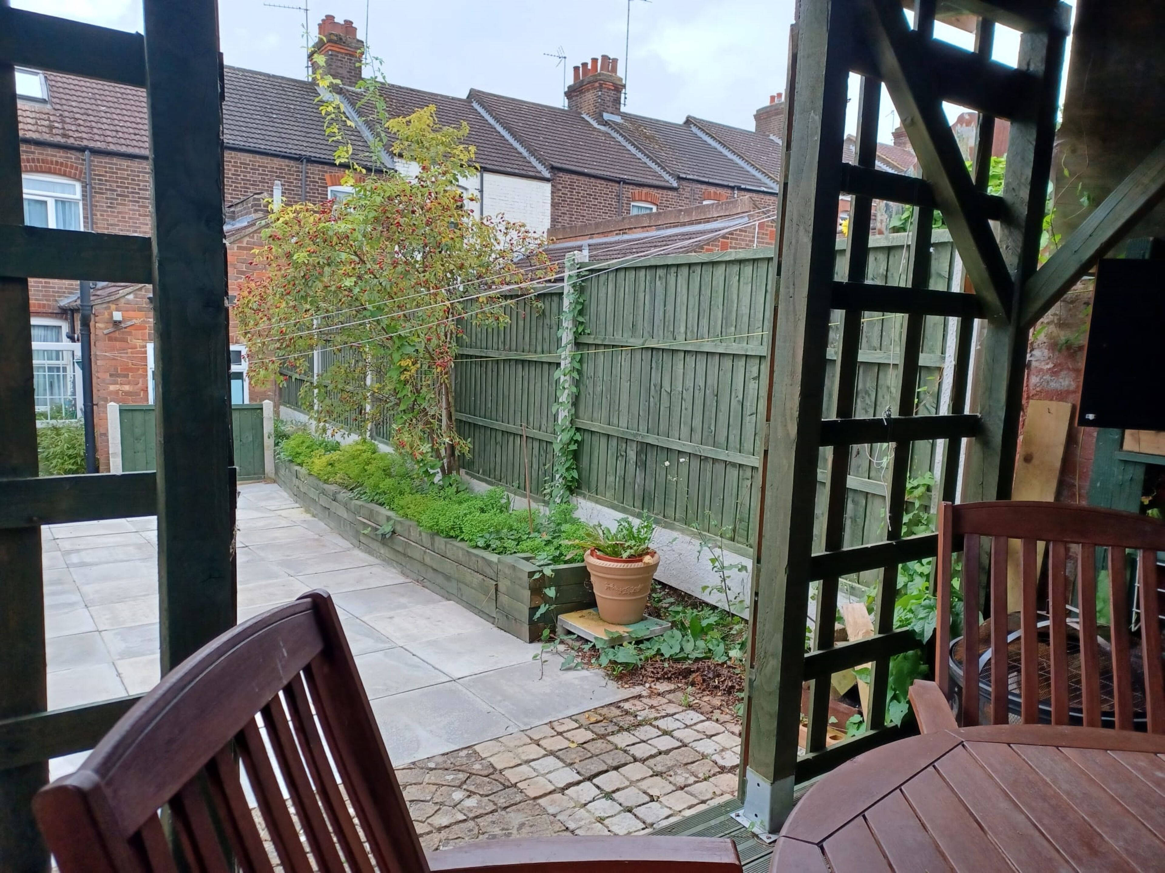 A patio area with a wooden table and chairs, a wooden fence, and a potted plant.