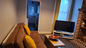 A living room with a sofa, a coffee table, a TV, and a brick fireplace. - Huku Kwetu - Ferndale House (Luton)