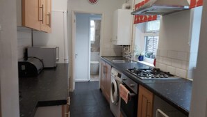 A narrow kitchen with a washing machine, a stove, and a sink. - Huku Kwetu - Ferndale House (Luton)