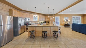 Una cocina moderna con armarios de madera, electrodomésticos de acero inoxidable, una isla central con taburetes y una zona de comedor con un sofá azul.
