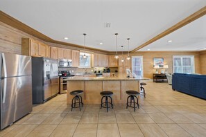 A modern kitchen with wooden cabinets, stainless steel appliances, a central island with stools, and a dining area with a blue sofa.