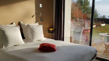 Una habitación de hotel con una cama grande, ropa de cama blanca, una almohada roja y vistas al exterior a través de un ventanal.