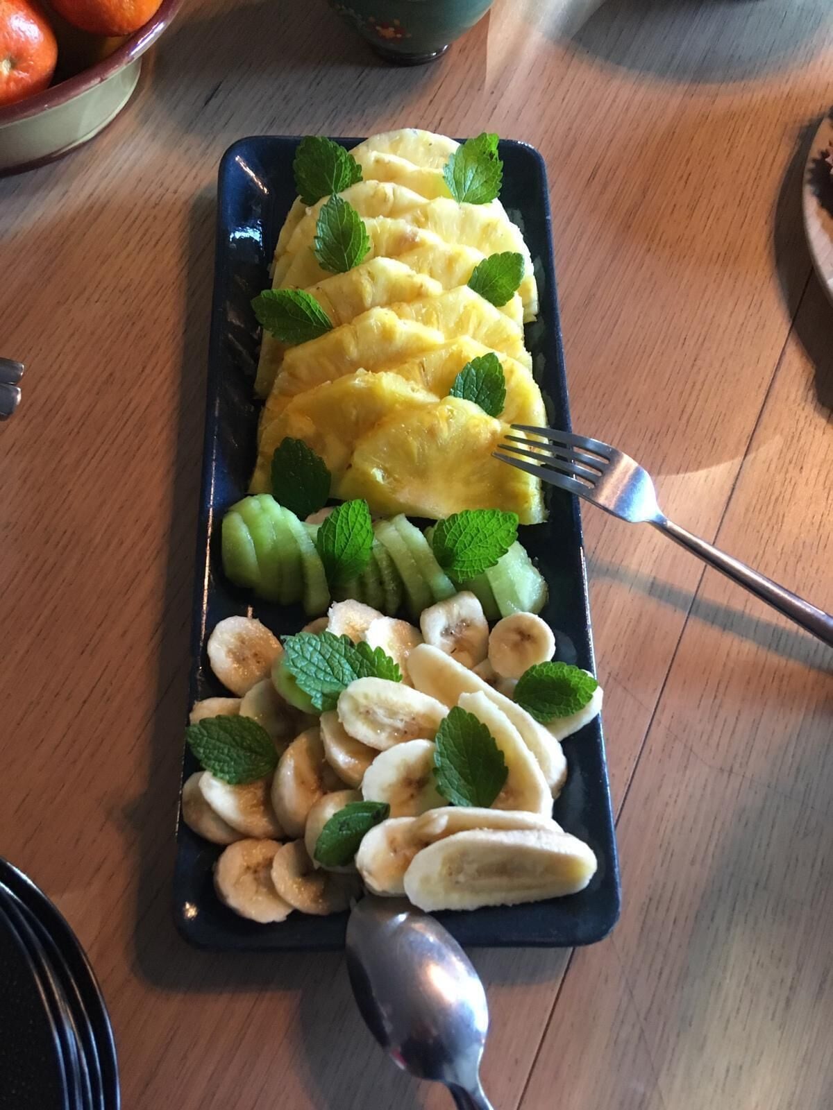 Une assiette rectangulaire contenant des tranches d’ananas, des rondelles de banane et des kiwis, posée sur une table en bois.