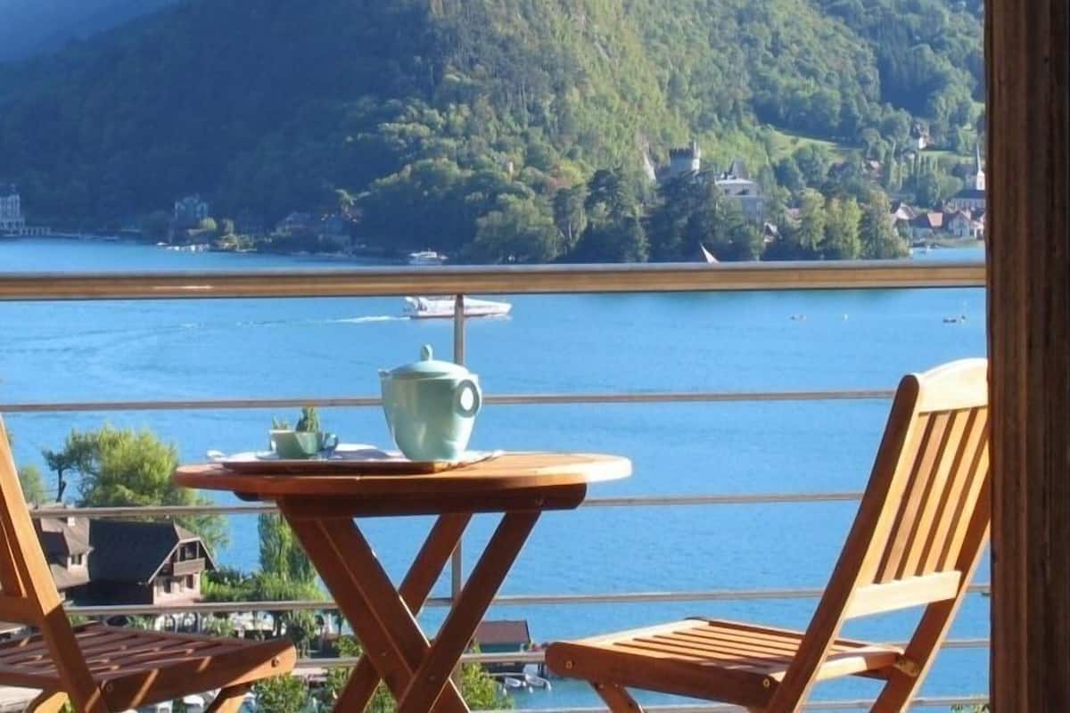 A balcony with a table and chairs overlooking a body of water and a mountainous landscape.
