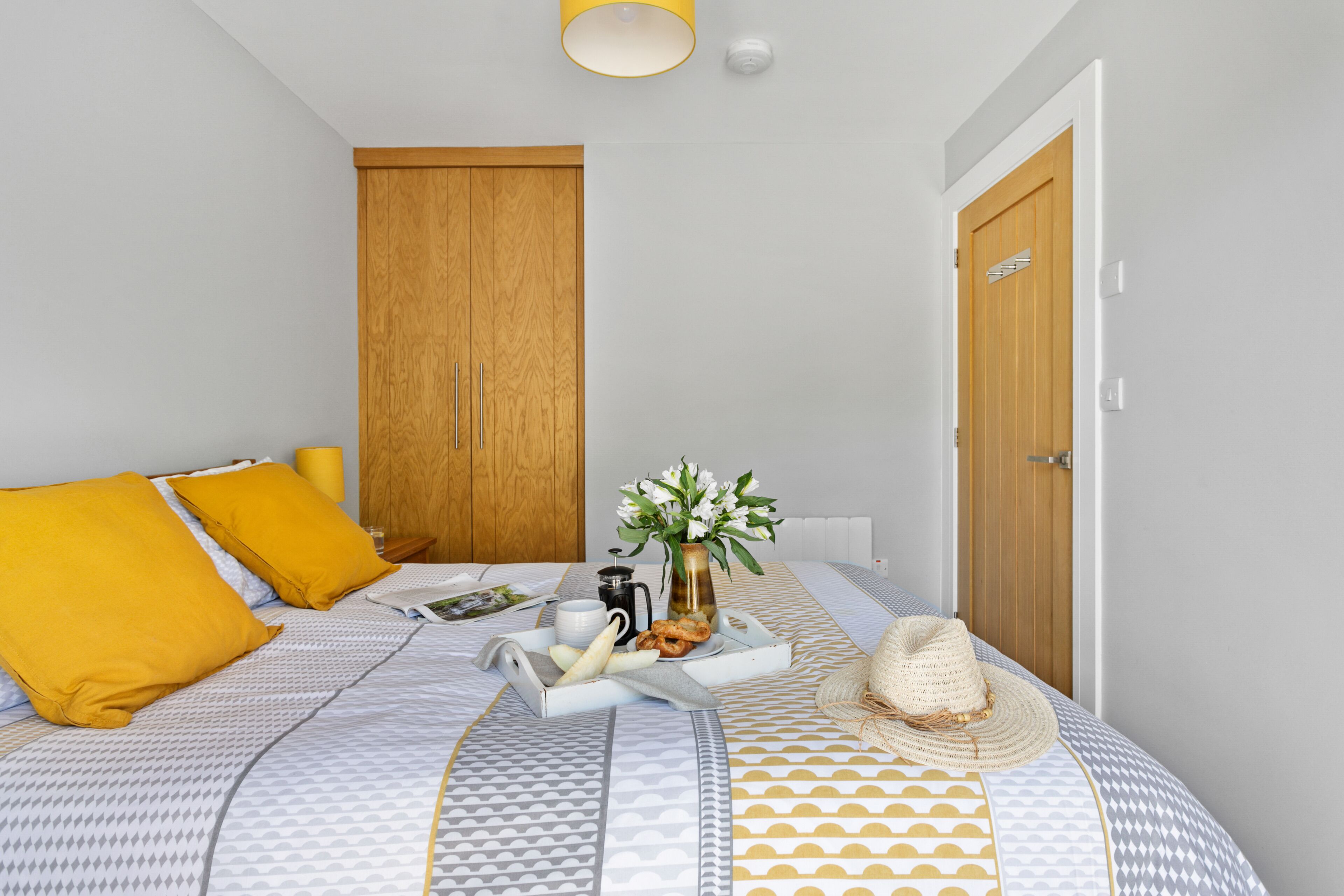 A neatly arranged bedroom with a bed, pillows, a bedside table with a vase, and a door.