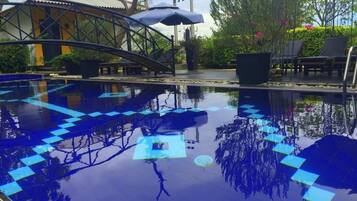 A swimming pool with a geometric tile pattern, surrounded by lounge chairs and umbrellas.