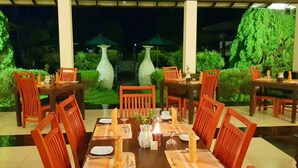 An outdoor dining area with tables and chairs, surrounded by greenery and decorative vases.