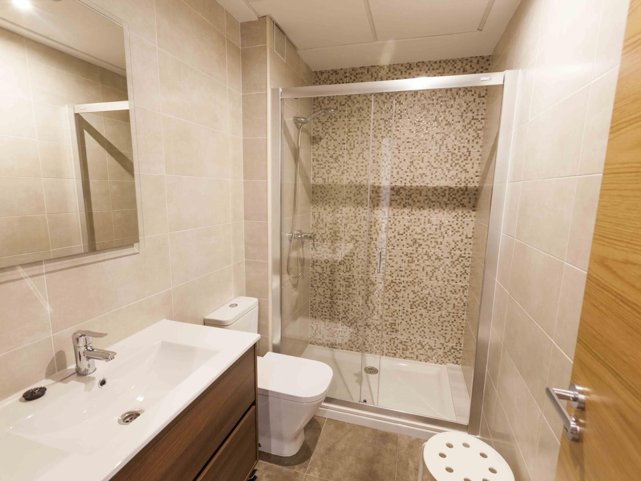 A bathroom with a shower, toilet, sink, and mirror.