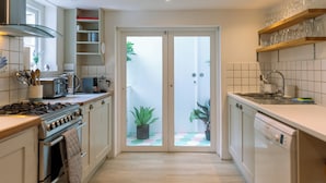 Eine moderne Küche mit Gaskochfeld, Backofen und Geschirrspüler, sowie eine Doppeltür zu einem Balkon mit Topfpflanzen.