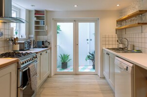 Une cuisine moderne équipée d’une cuisinière à gaz, d’un four et d’un lave-vaisselle, avec une porte-fenêtre donnant sur un balcon agrémenté de plantes en pot.