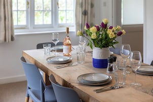 A dining table set with plates, cutlery, glasses, and a bottle of wine, with a vase of flowers on the table.